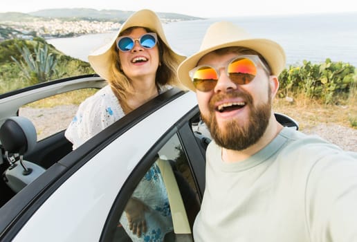 Happy beautiful couple in love taking a selfie portrait driving a convertible car on the road at vacation. Rental cars and vacation concept