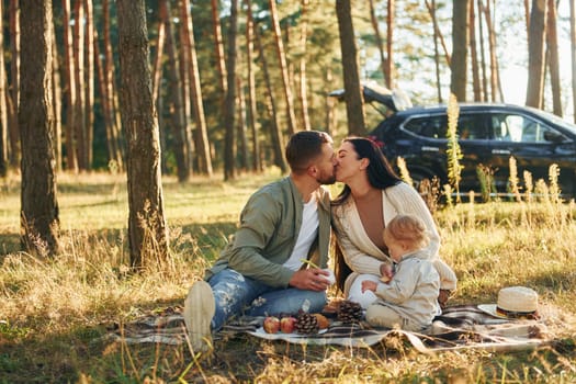 Kissing each other. Happy family of father, mother and little daughter is in the forest.