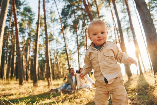 Little girl is running. Happy family of father, mother and little daughter is in the forest.