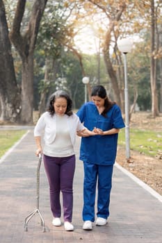 nurse helping elderly woman with walker Nurse holding hand and help elderly woman walking in park facility.