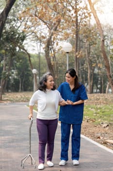 nurse helping elderly woman with walker Nurse holding hand and help elderly woman walking in park facility.