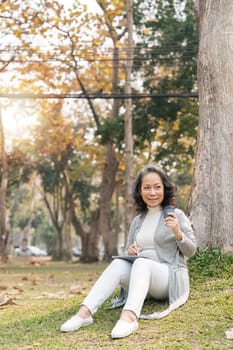 Asia grandmother 60s using tablet vacation watching Social news holiday in park and sip coffee.