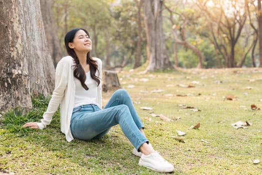 happy Asian woman sitting on grass in the green park, relaxing with nature in the park.