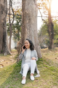 Happy senior woman at park using mobile phone. Cute elderly woman receive a message phone for her beloved.