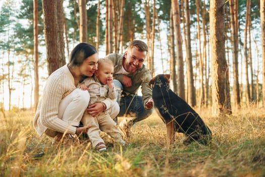 Playing with dog. Happy family of father, mother and little daughter is in the forest.