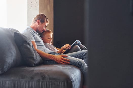 Sitting on the sofa. Father and son is indoors at home together.