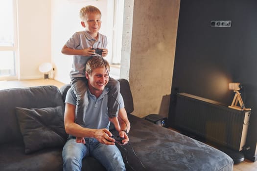 Playing video game. Father and son is indoors at home together.