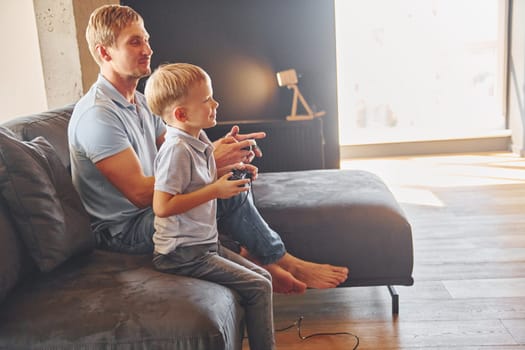 Playing video game. Father and son is indoors at home together.
