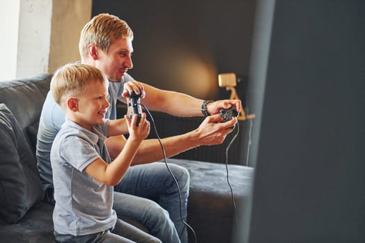 Holding video game controllers. Father and son is indoors at home together.