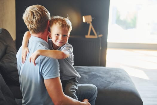 Boy embracing his parent. Father and son is indoors at home together.