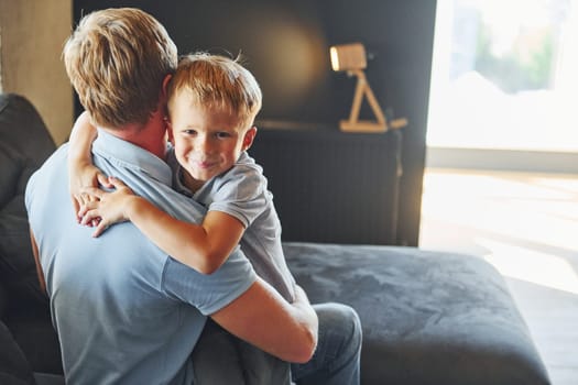 Boy embracing his parent. Father and son is indoors at home together.