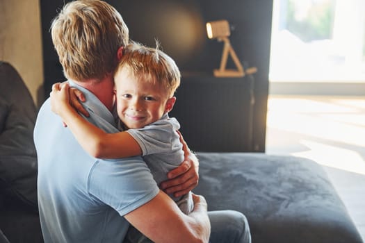 Boy embracing his parent. Father and son is indoors at home together.