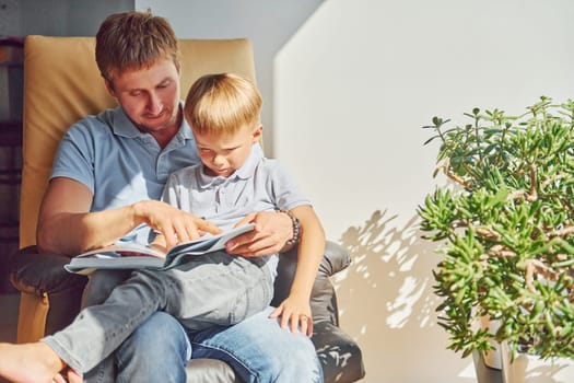 Sitting with book. Beautiful sunlight. Father and son is indoors at home together.