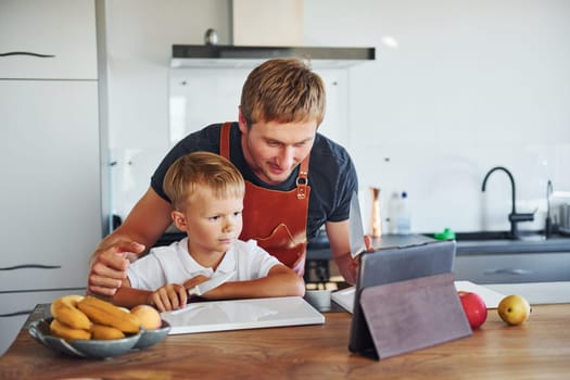 Learning how to cook. Father and son is indoors at home together.