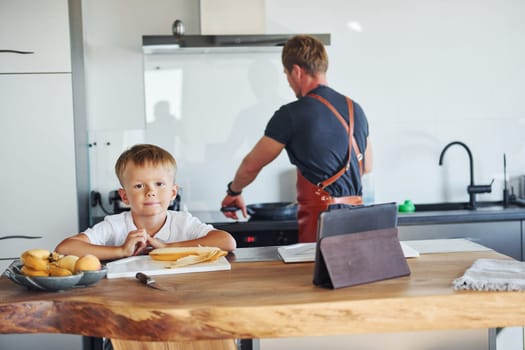 Learning how to cook. Father and son is indoors at home together.