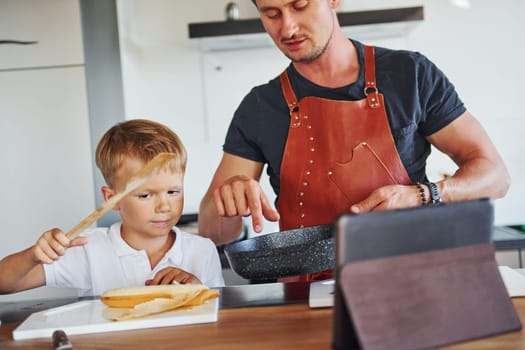 Learning how to cook. Father and son is indoors at home together.