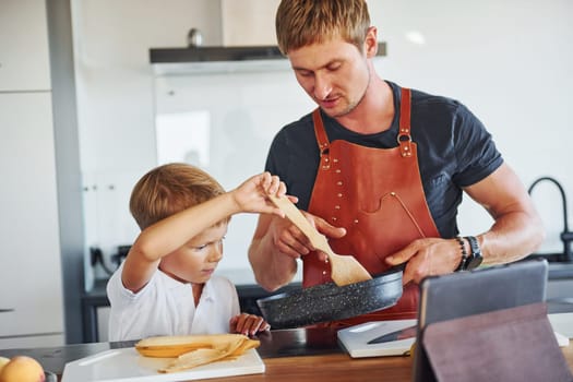 Using tablet to learn how to cook. Father and son is indoors at home together.