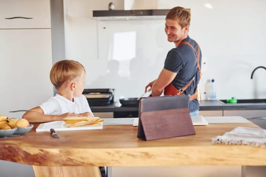 Using tablet to learn how to cook. Father and son is indoors at home together.