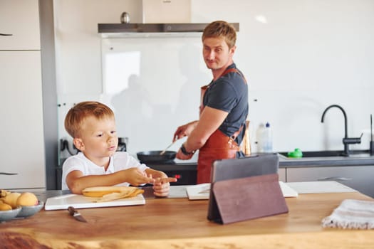 Using tablet to learn how to cook. Father and son is indoors at home together.