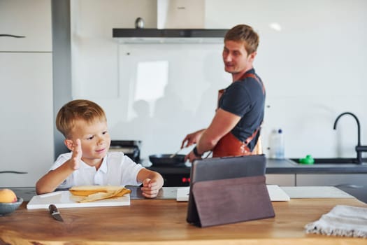 Using tablet to learn how to cook. Father and son is indoors at home together.