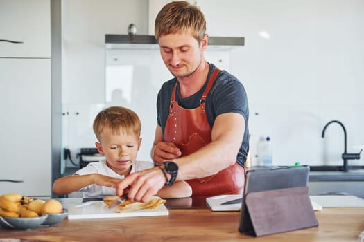 On the kitchen with food. Father and son is indoors at home together.