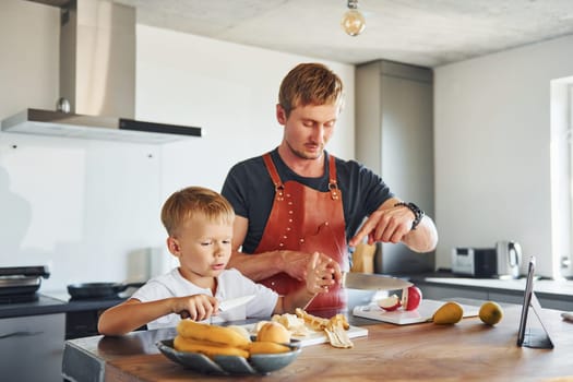 On the kitchen with food. Father and son is indoors at home together.