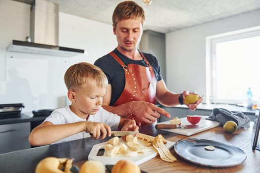 Man is in the apron on kitchen. Father and son is indoors at home together.