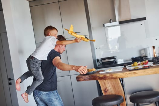 Playing with yellow toy plane. Father and son is indoors at home together.