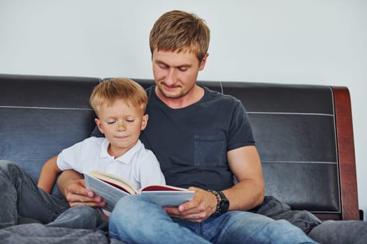 With book in hands. Father and son is indoors at home together.