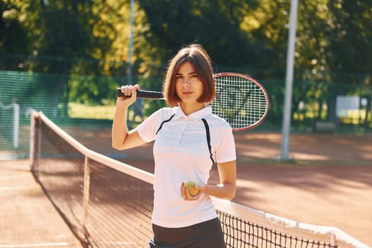 Standing with racket in hand. Female tennis player is on the court at daytime.