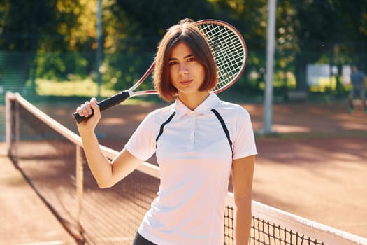 Standing with racket in hand. Female tennis player is on the court at daytime.