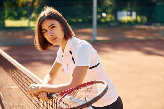 Standing with racket in hand. Female tennis player is on the court at daytime.