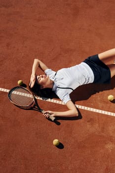 Laying down on the ground. Female tennis player is on the court at daytime.
