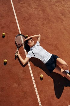 Laying down on the ground. Female tennis player is on the court at daytime.