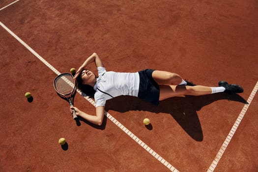 Laying down on the ground. Female tennis player is on the court at daytime.