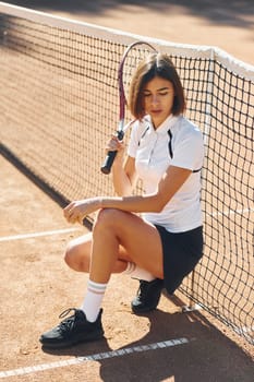 Sitting and posing. Female tennis player is on the court at daytime.