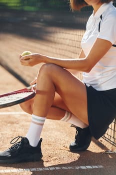 Sitting and holding racket. Female tennis player is on the court at daytime.