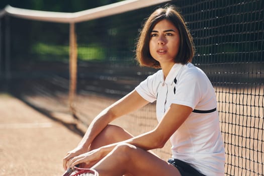 Looking at the camera. Female tennis player is on the court at daytime.