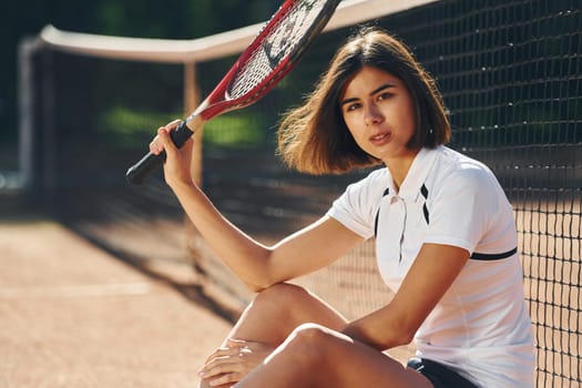 Looking at the camera. Female tennis player is on the court at daytime.