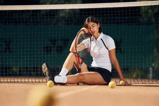Sitting near the net. Female tennis player is on the court at daytime.