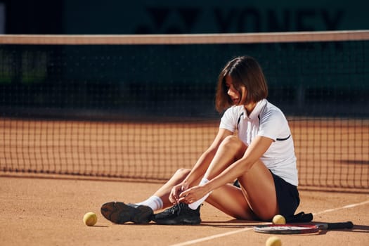 In white shirt and black skirt. Female tennis player is on the court at daytime.