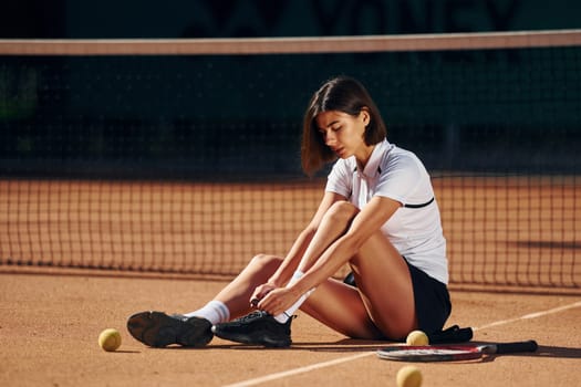 In white shirt and black skirt. Female tennis player is on the court at daytime.