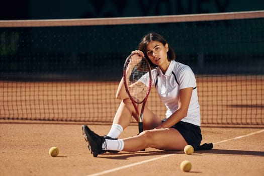In white shirt and black skirt. Female tennis player is on the court at daytime.