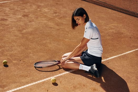 On the ground. Female tennis player is on the court at daytime.