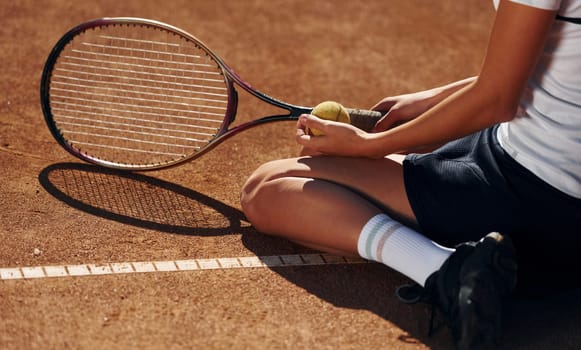 On the ground. Female tennis player is on the court at daytime.