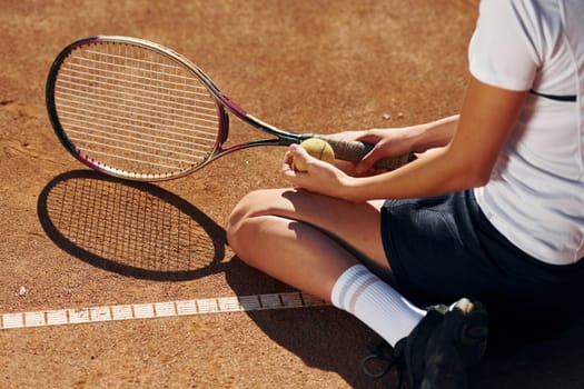 On the ground. Female tennis player is on the court at daytime.