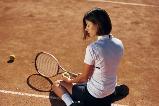 Taking a break. Female tennis player is on the court at daytime.