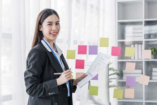 Young businesswoman creative team using post it notes in glass wall to writing strategy business plan to development grow to success...