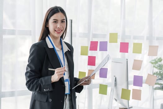 Young businesswoman creative team using post it notes in glass wall to writing strategy business plan to development grow to success...