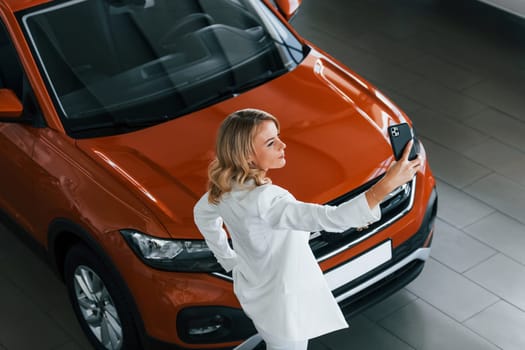 Making selfie. Woman in formal clothes is indoors in the autosalon.